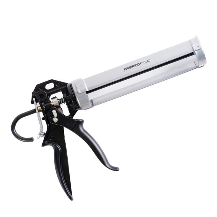 Hardtouch Duo A silver and black caulking gun placed on a surface, with a pair of scissors nearby.