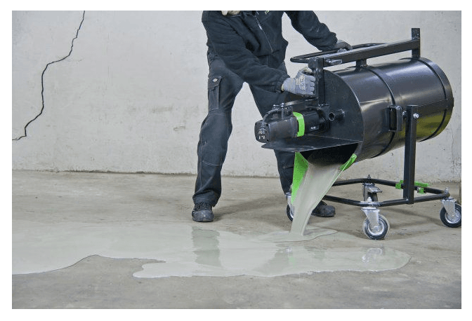 Mixing-spill-1.png A person in dark clothing operates a machine that is pouring a liquid substance onto a concrete floor.