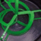 A green metal device with several loops and rods placed inside a black circular container.